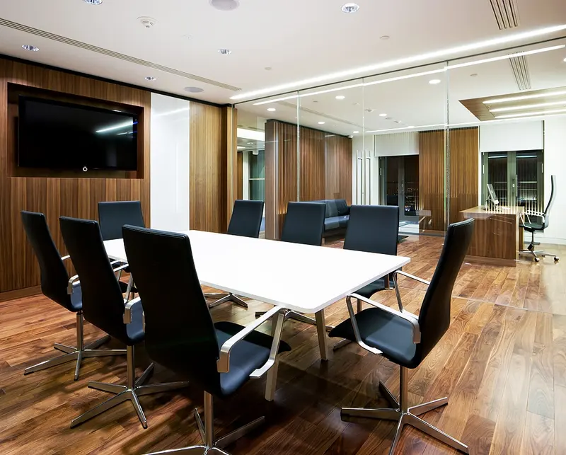 Sala de reuniões com mesa branca, painel de TV e revestimento de madeira